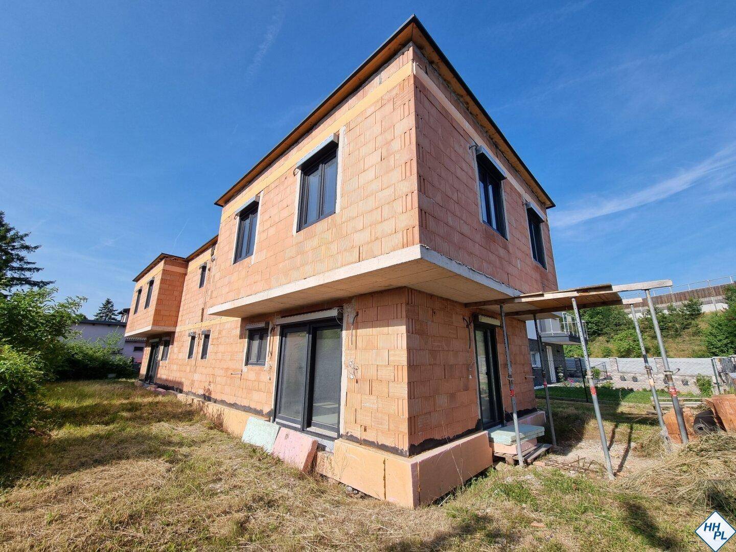 Seitenansicht des Neubaus im Rohbau mit Ziegelmauerwerk und installierten Fenstern.