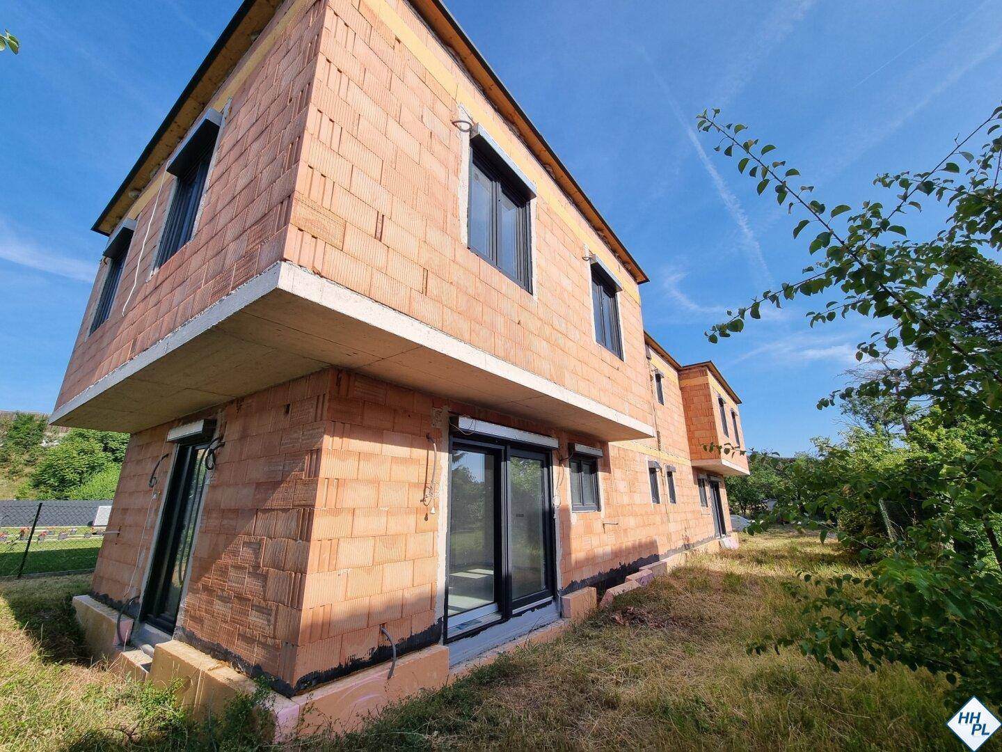 Schräge Ansicht des Neubaus im Rohbau mit Ziegelmauerwerk und großen Fensteröffnungen.