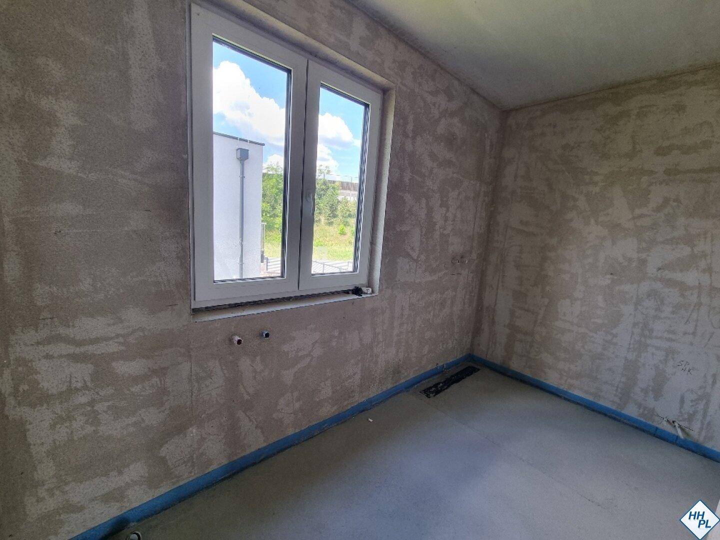 Unfertiger Raum mit Estrichboden und einem Fenster, das Tageslicht hereinlässt.
