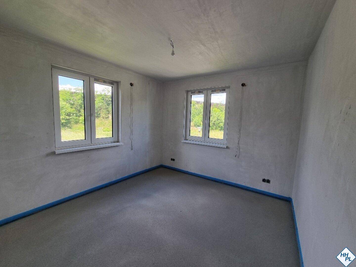 Unfertiges Schlafzimmer mit Estrichboden und zwei Fenstern, die viel Tageslicht hereinlassen.