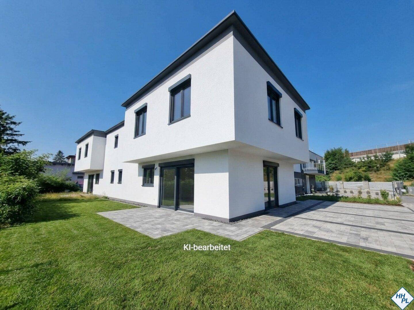 Ansicht eines modernen Neubaus mit weißer Fassade, gepflasterter Zufahrt und grünem Rasen.
