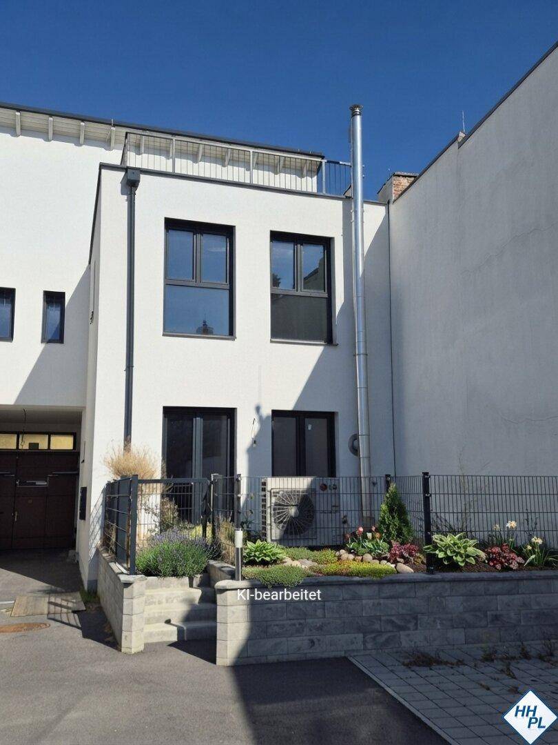 Moderne weiße Fassade eines Reihenhauses mit dunklen Fenstern, kleinem Vorgarten und Dachterrasse.