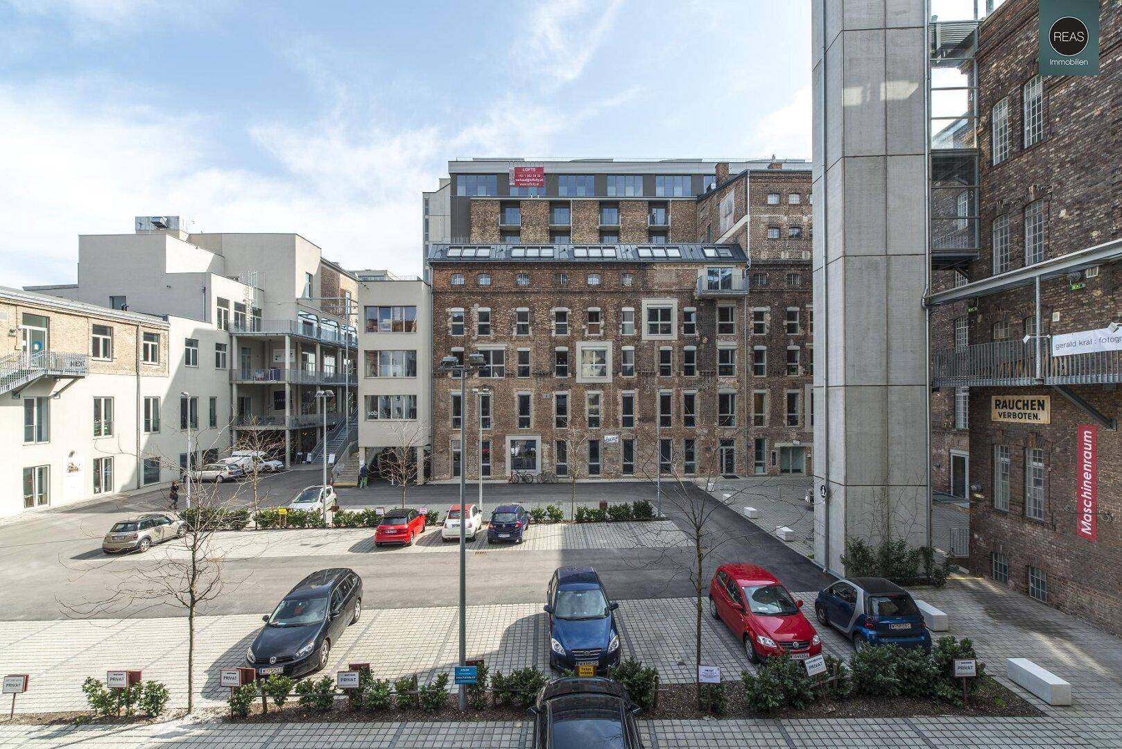 Außenansicht eines Gebäudekomplexes mit Parkplätzen und historischer Backsteinfassade.