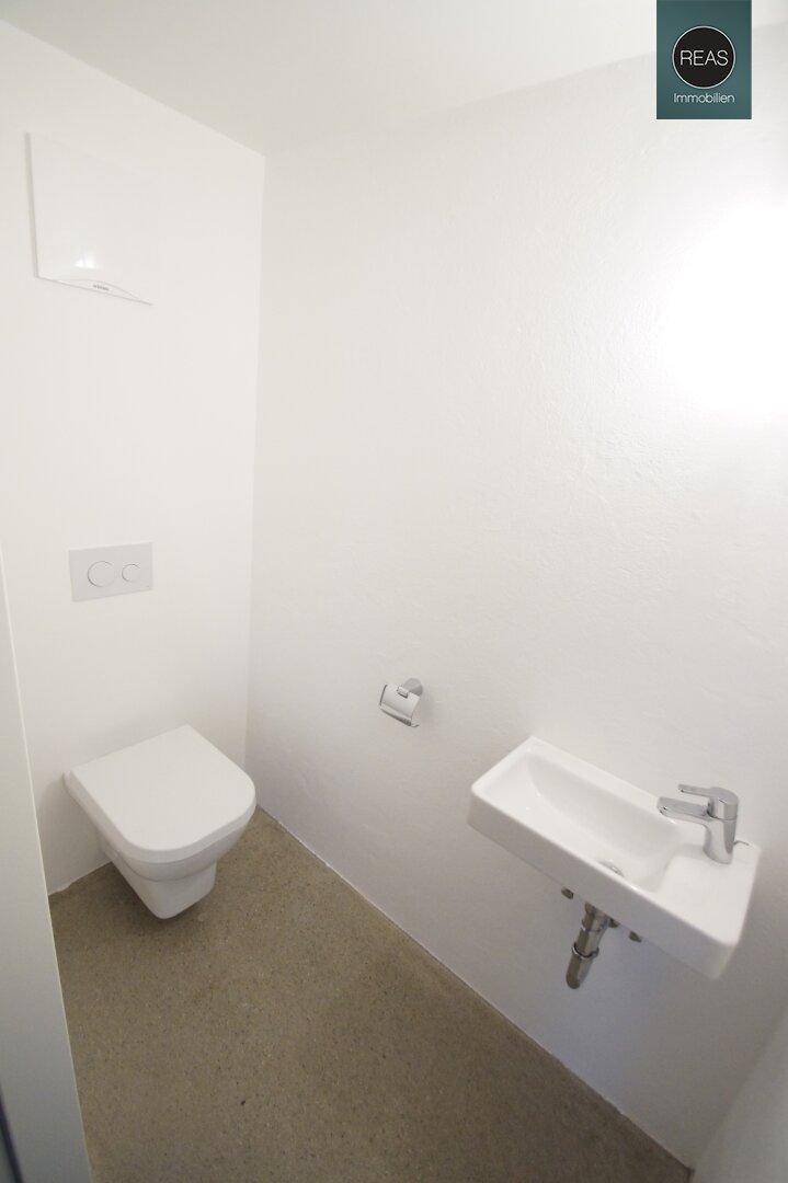 Helle Gästetoilette mit wandhängendem WC und kleinem Waschbecken.