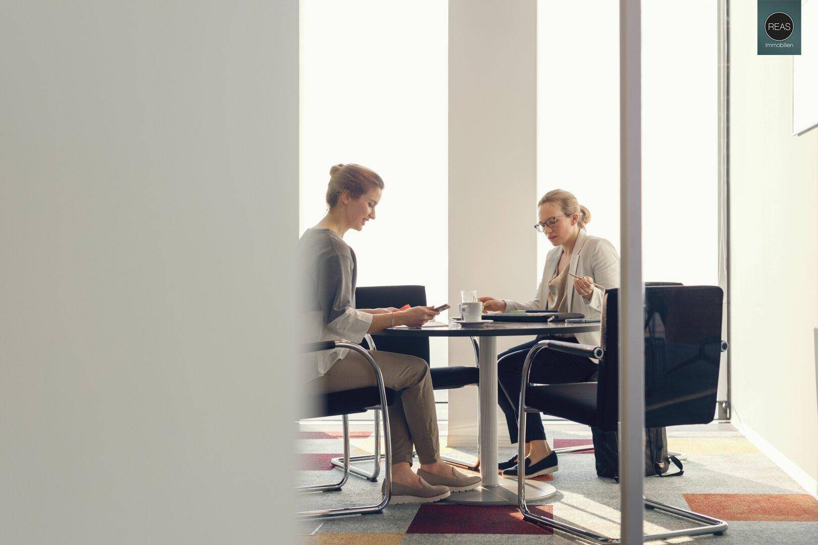 Zwei Frauen sitzen an einem runden Tisch in einem hellen Besprechungsraum.