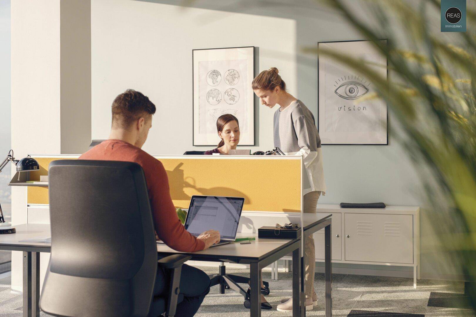 Drei Personen in einem modernen Büro mit gelben Trennwänden und dekorativen Bildern an der Wand.