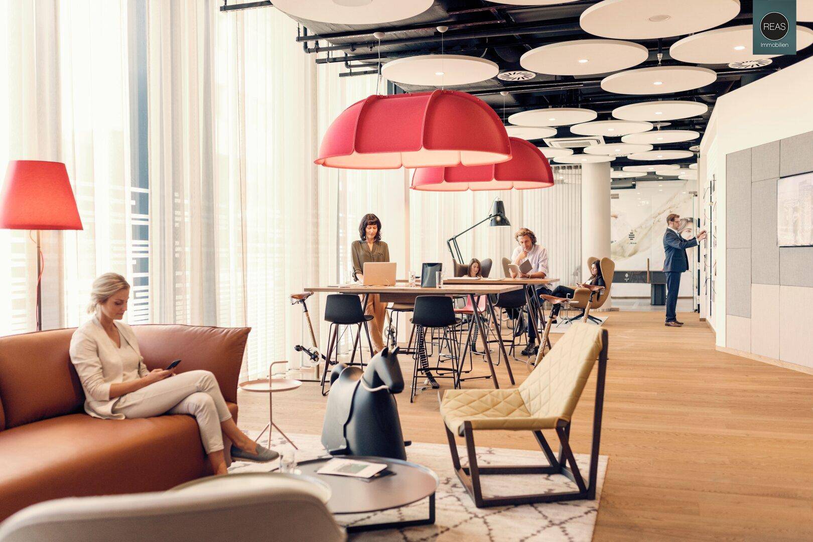 Offener Lounge-Bereich mit Holzboden, roten Lampen und verschiedenen Arbeitsbereichen.