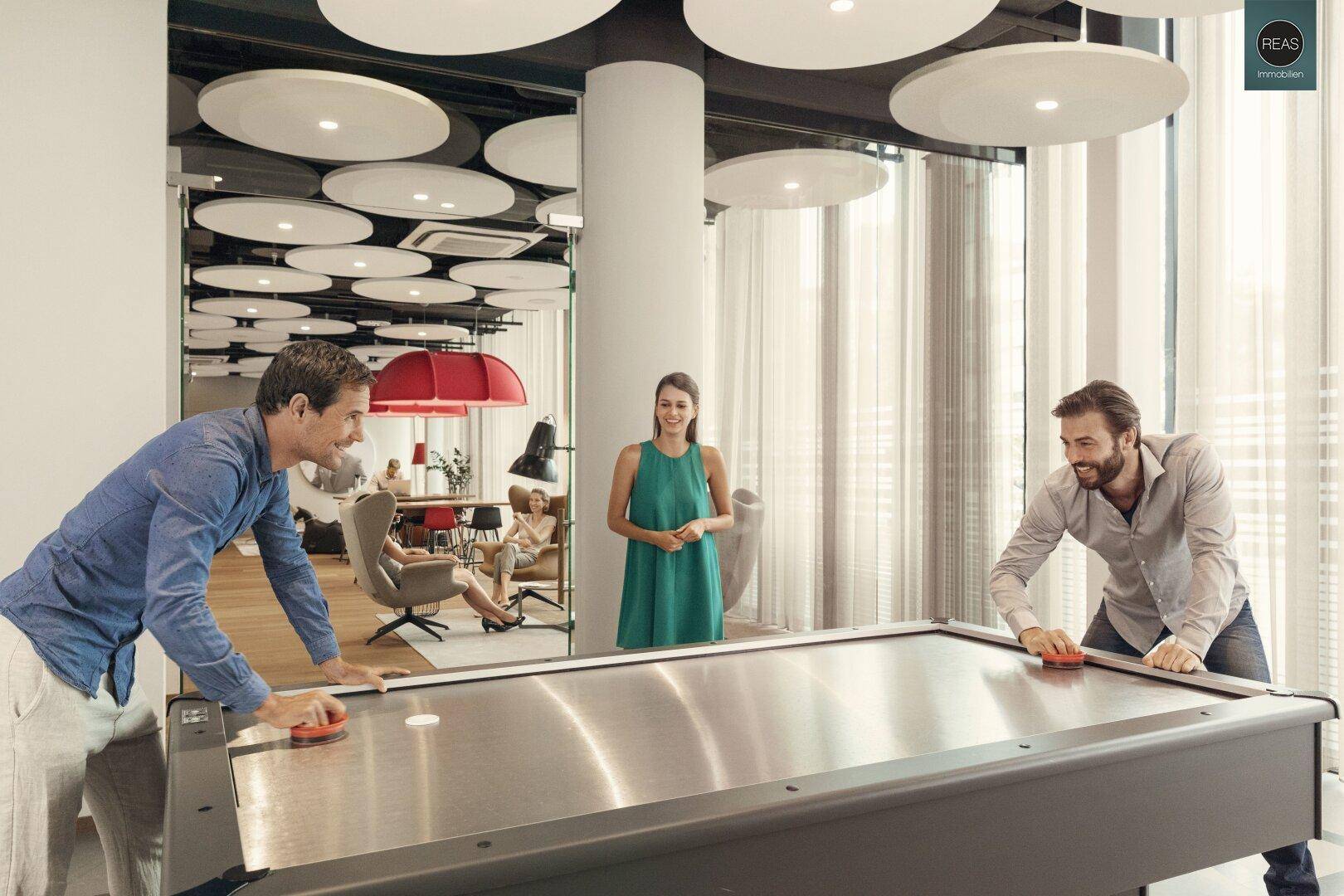 Zwei Männer spielen Airhockey in einem modernen Freizeitraum mit Lounge-Bereich.