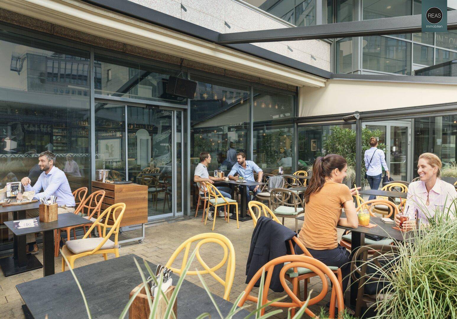 Gemütliche Außenterrasse eines Cafés mit Tischen, Stühlen und Pflanzen.