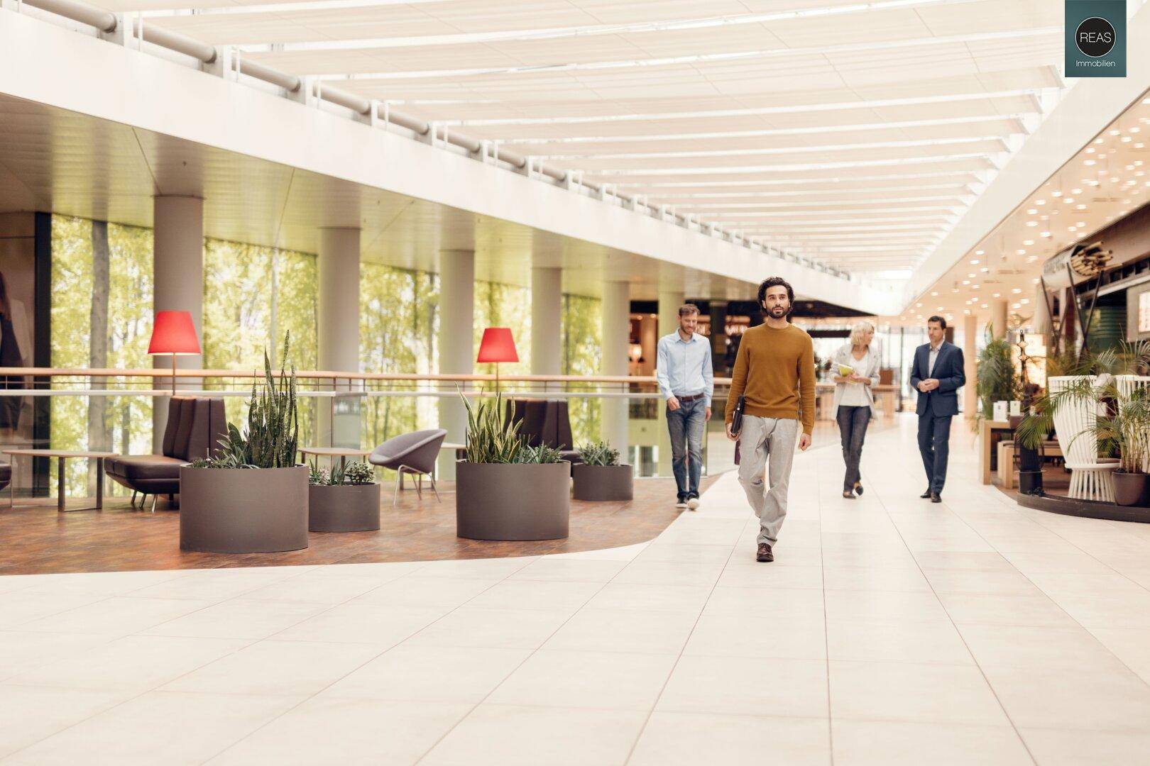 Helle, moderne Ladenpassage mit breitem Gang und Pflanzen als Dekoration.