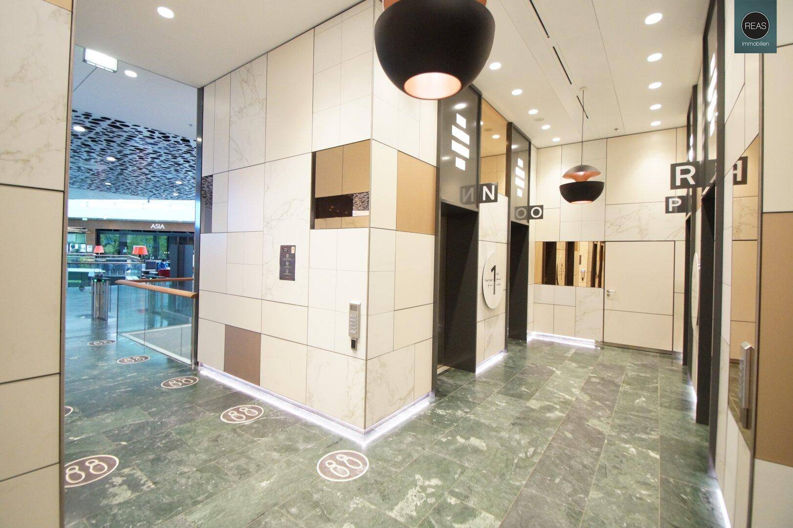 Elegante Lobby mit Marmorboden, Aufzügen und modernen Deckenleuchten.