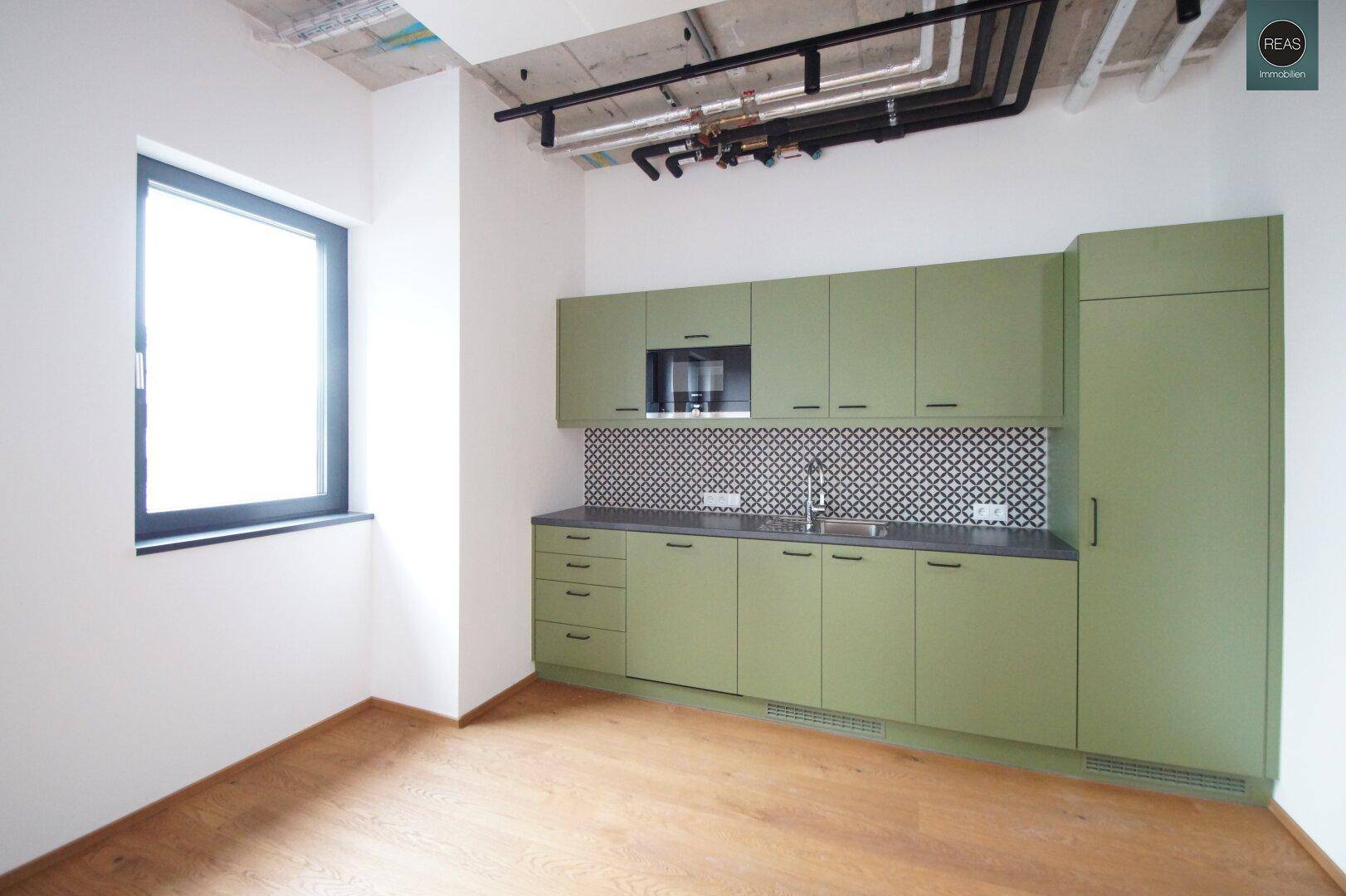 Funktionale Küchenzeile mit grünen Schränken und Fenster, ideal für die Versorgung im Büroalltag.