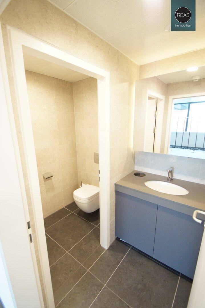 Modernes WC mit dunklen Fliesen und hellem Waschtisch, sauber und funktional.