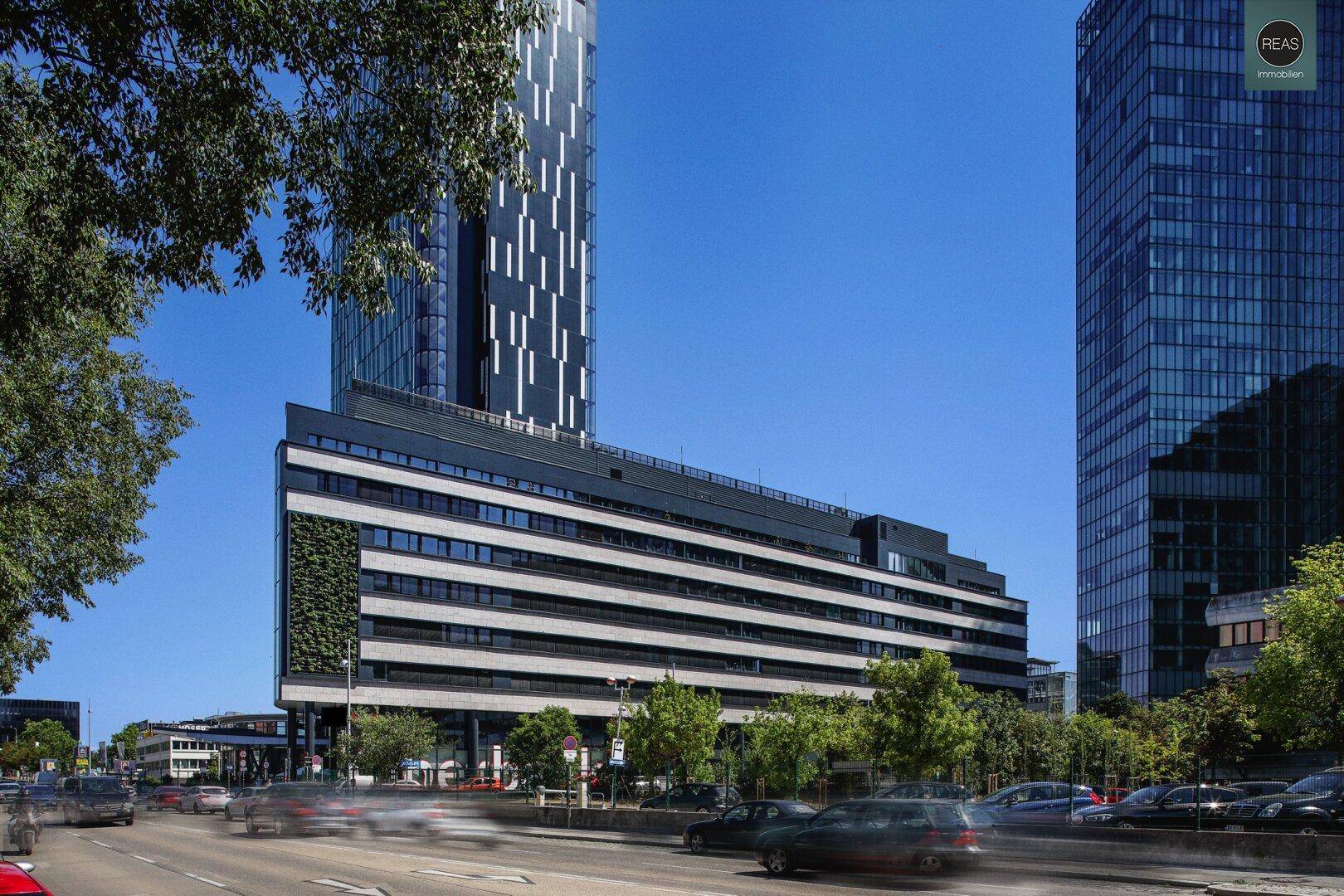 Moderne Bürogebäude mit vertikaler Begrünung und belebter Straße, integriert in die städtische Umgebung.