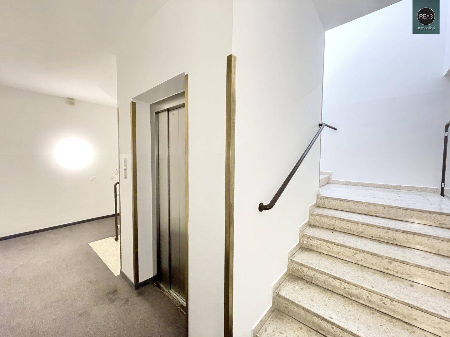 Treppenhaus mit Marmorstufen und einem Aufzug, der Zugang zu den verschiedenen Etagen bietet.