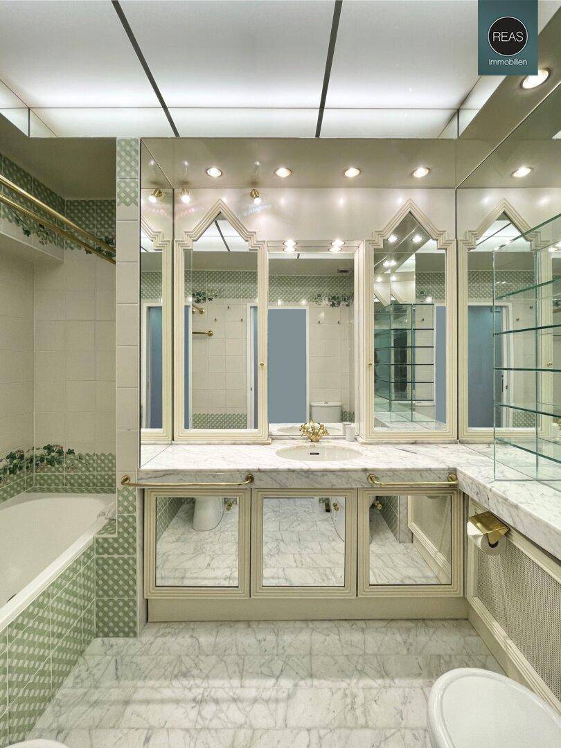 Klassisches Badezimmer mit Marmorboden, grünen Fliesen und einer Badewanne, umgeben von Spiegeln.