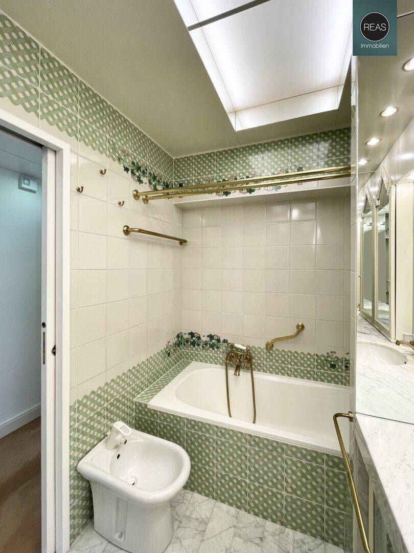 Badezimmer mit Badewanne, Bidet und grünen Fliesen, ausgestattet mit praktischen Haltegriffen.