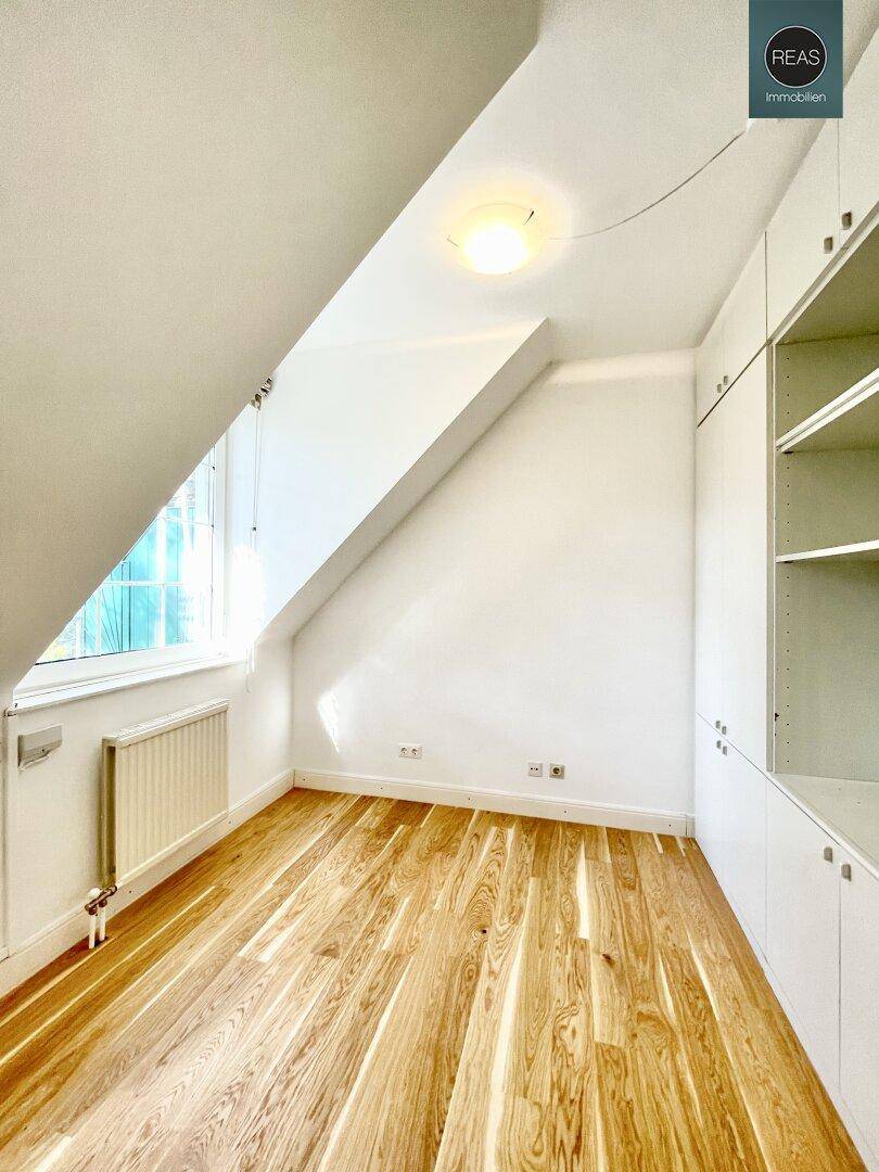 Kleines, helles Zimmer im Dachgeschoss mit Holzboden, schrägen Wänden und praktischen Einbauregalen.