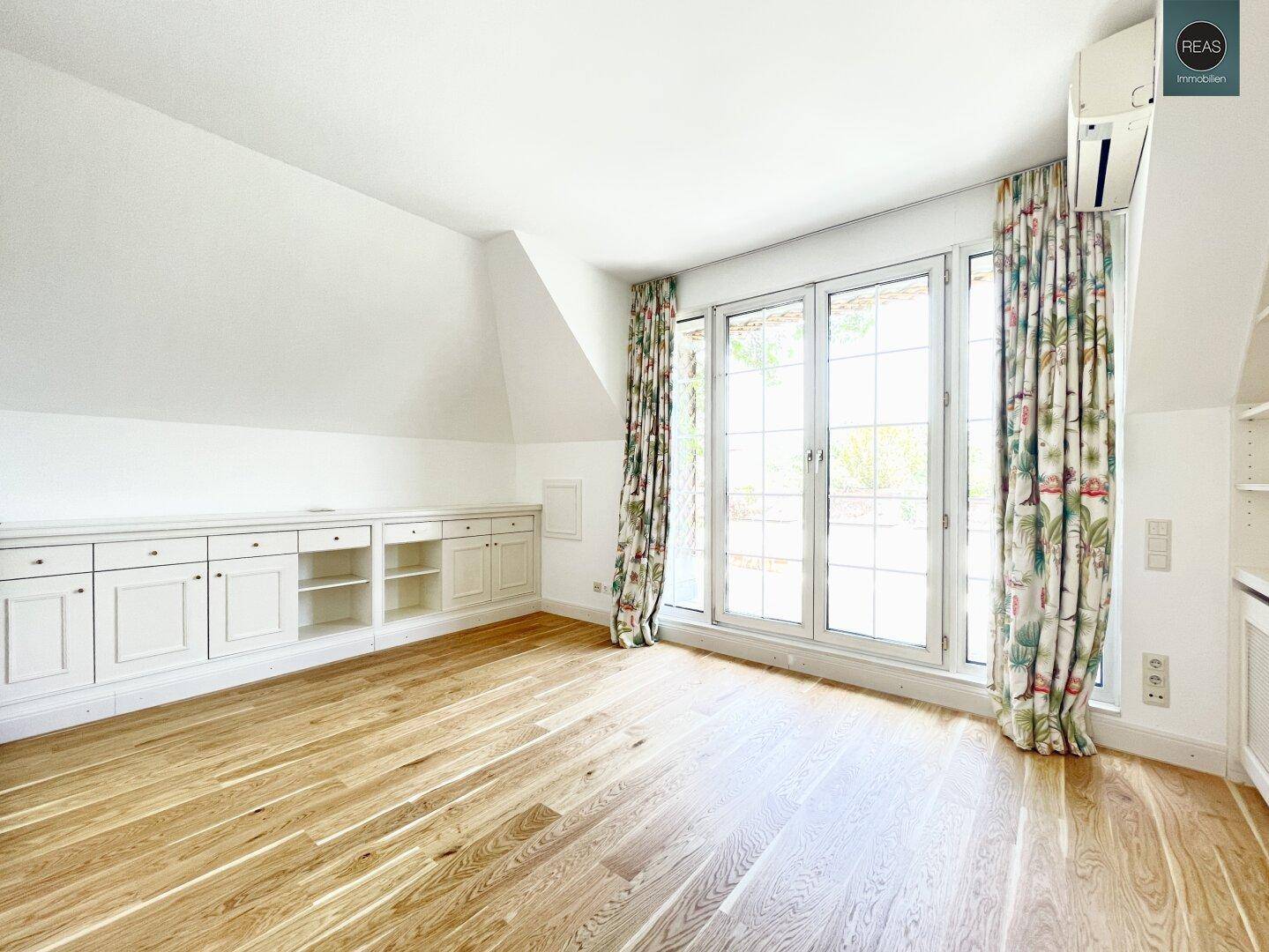 Helles Schlafzimmer mit Holzboden, Einbauschränken und Zugang zur sonnigen Terrasse.