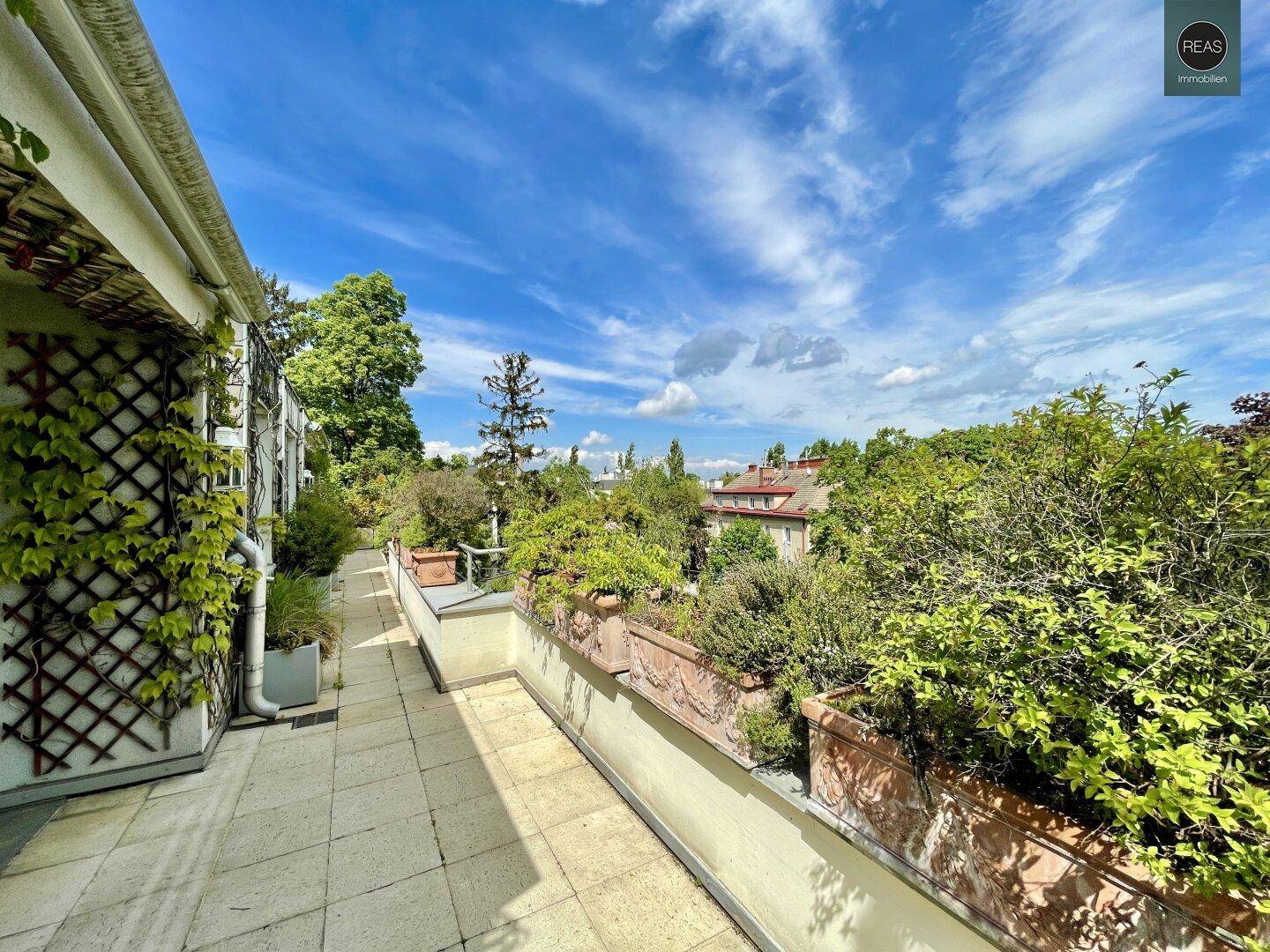 Lange Terrasse mit Fliesenboden, üppiger Bepflanzung und weitem Blick über die Umgebung.