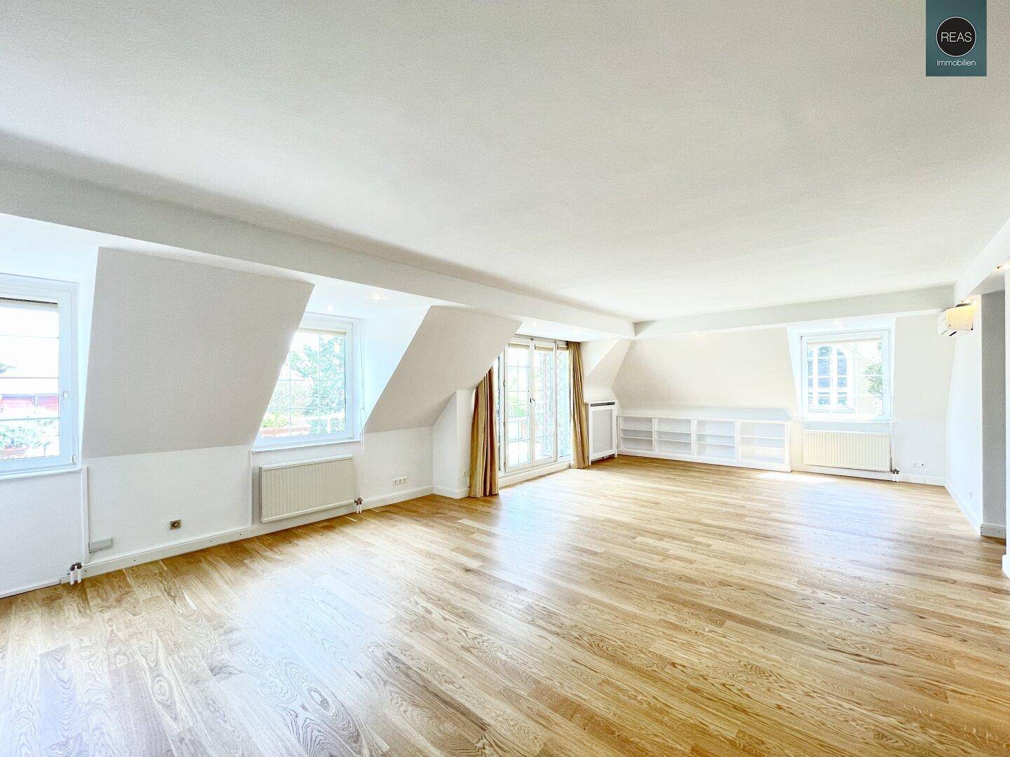 Großer, heller Wohnraum mit Holzboden, Dachschrägenfenstern und Klimaanlage.