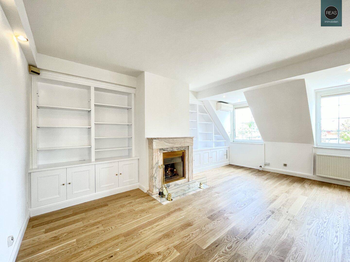 Gemütlicher Wohnbereich mit Marmorkamin, Holzboden und eingebauten Bücherregalen.
