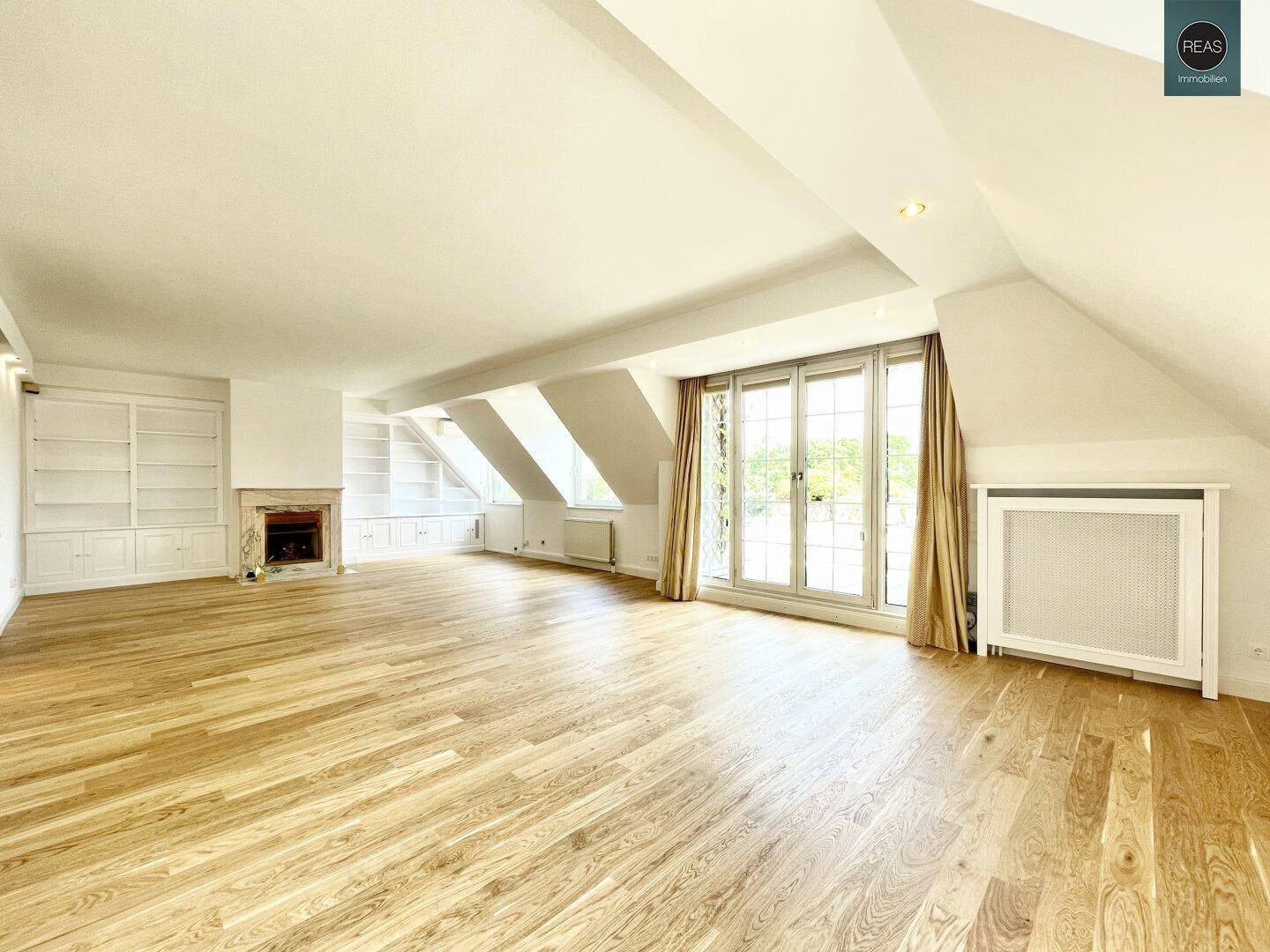 Heller, leerer Wohnbereich mit Holzboden, Kamin und eingebauten Regalen unter der Dachschräge.