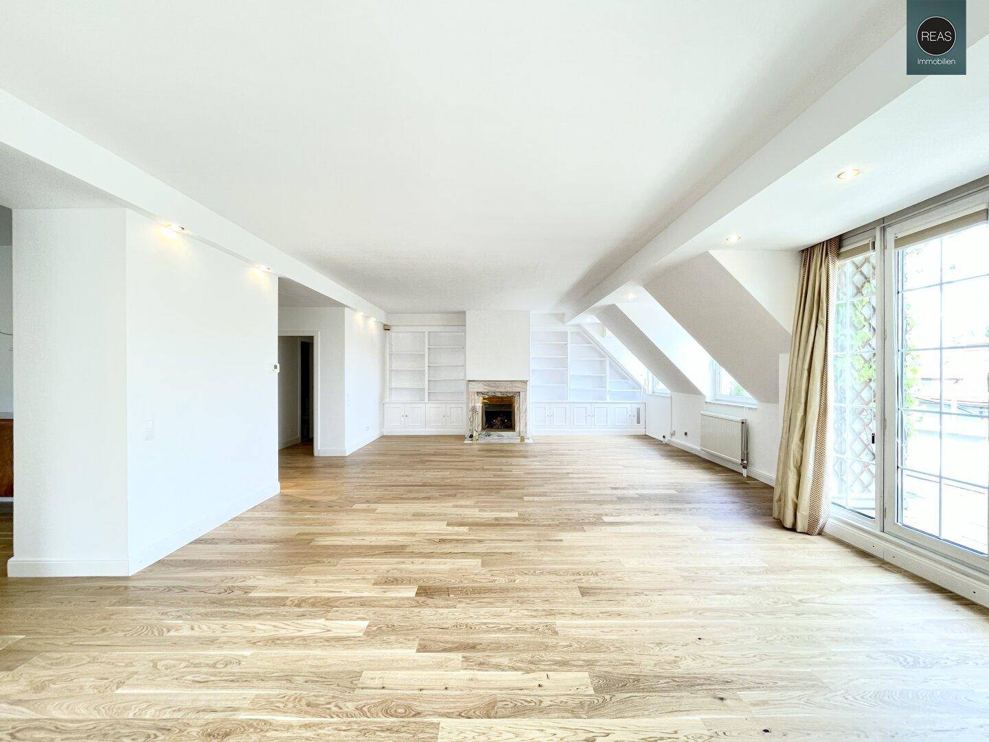 Großer, heller Wohnraum mit Holzboden, Kamin und eingebauten Regalen unter der Dachschräge.