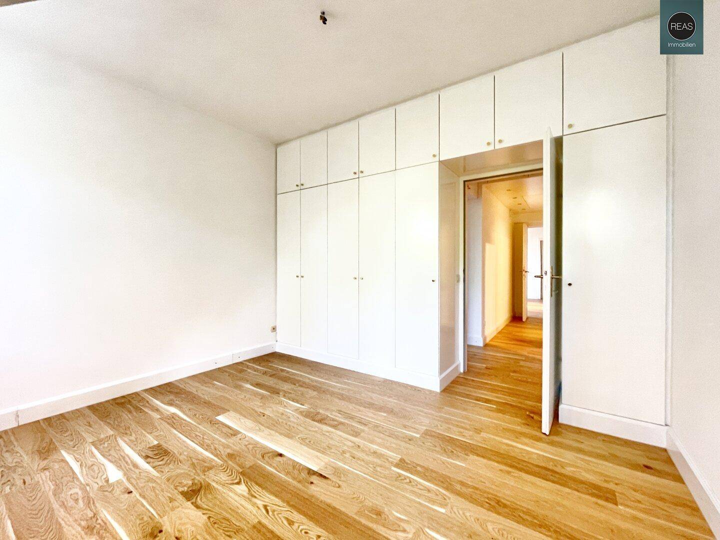 Geräumiges Zimmer mit Holzboden und einer Wand voller weißer Einbauschränke, die viel Stauraum bieten.