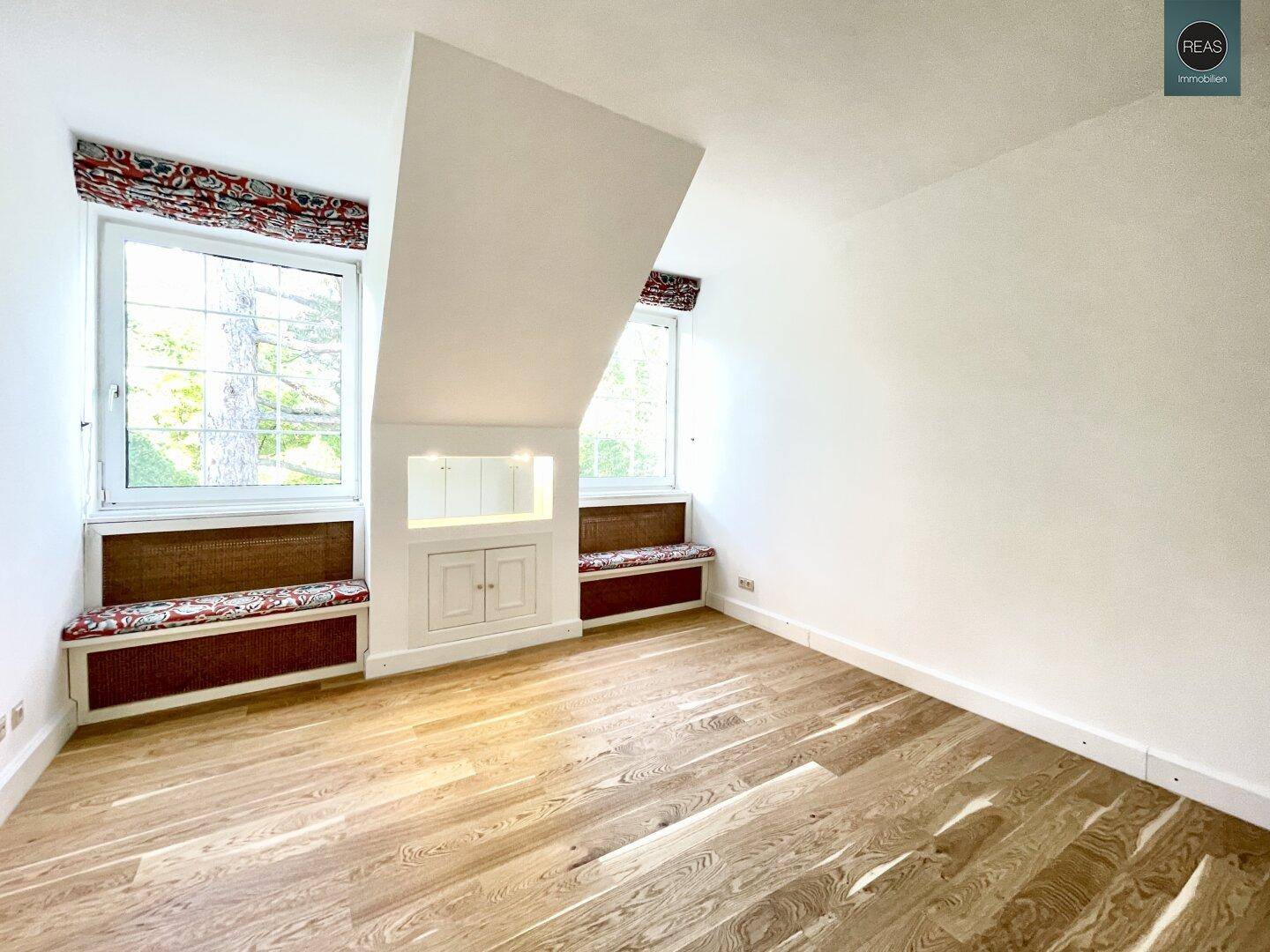 Helles Zimmer im Dachgeschoss mit Holzboden, schrägen Wänden und integrierten Fensterbänken.