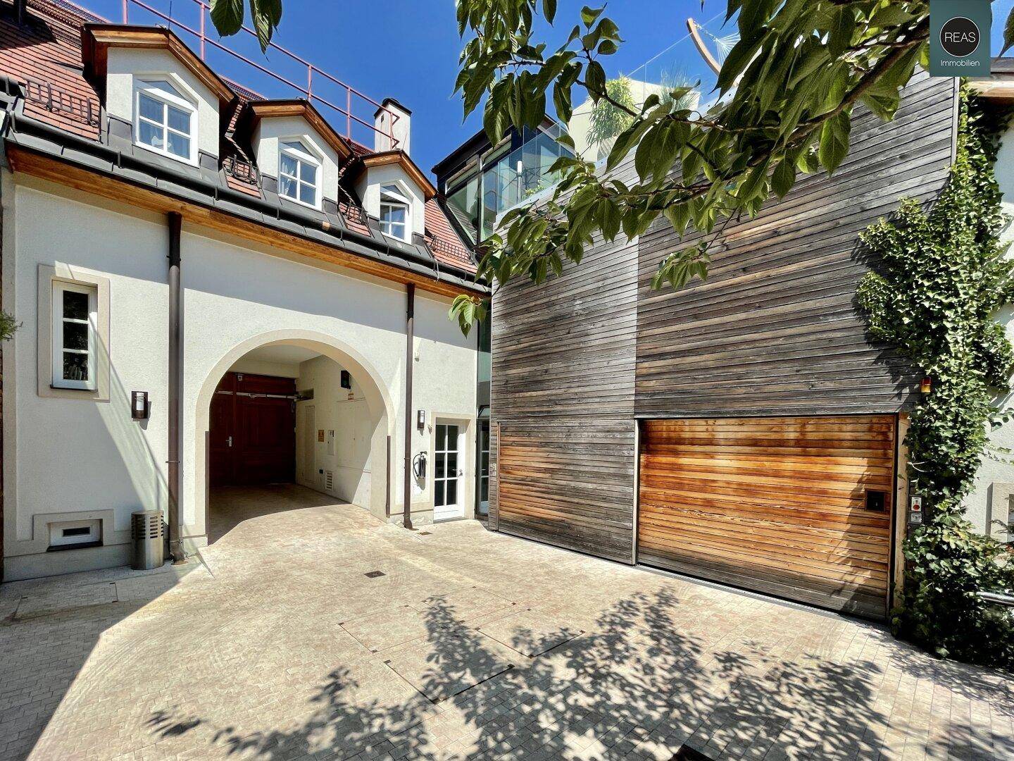 Kombination aus moderner Holzfassade und traditionellem Gebäude mit gepflastertem Hof und üppigem Grün.