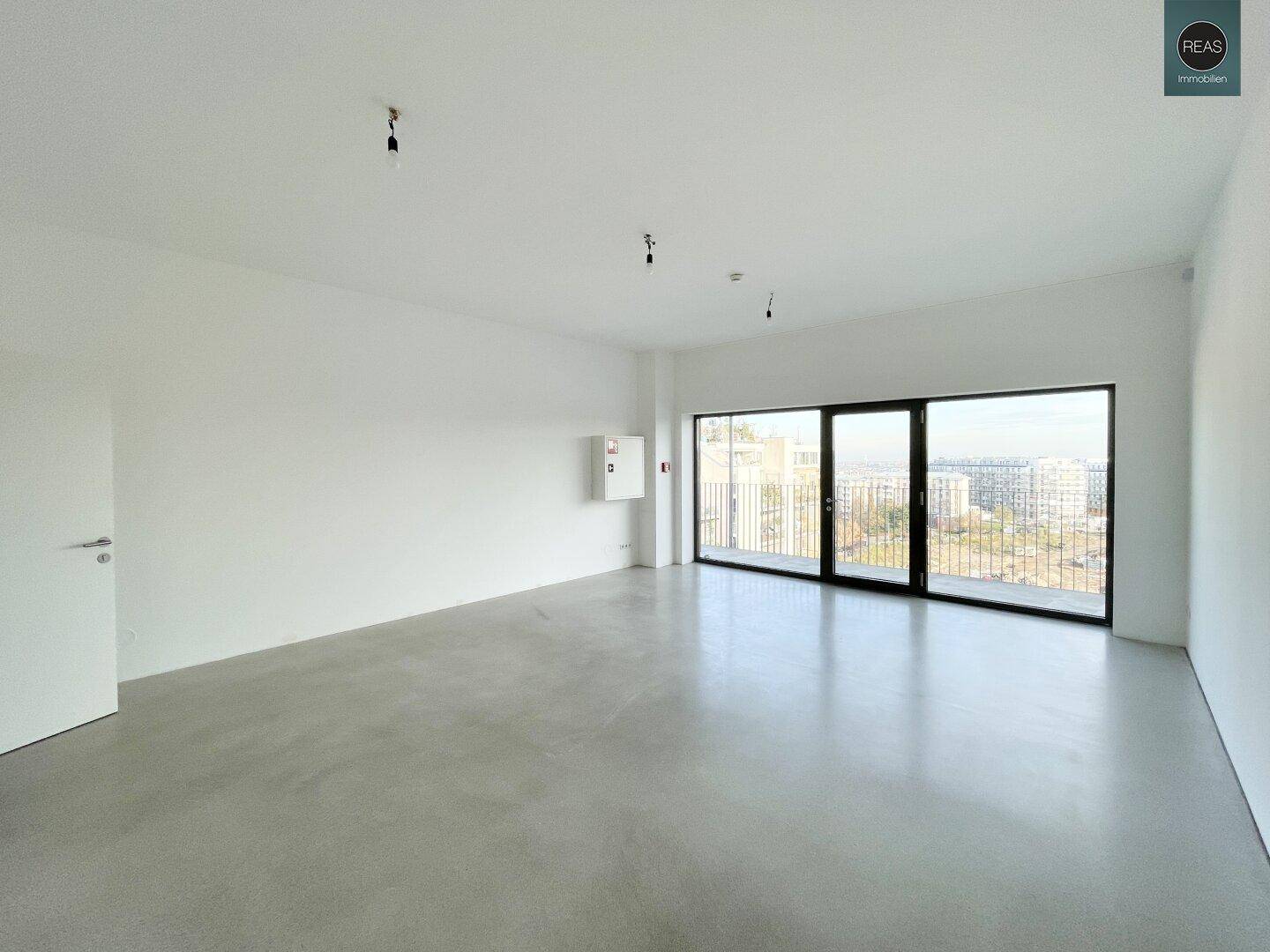 Heller, leerer Büroraum mit Betonboden und großen Fenstern, die viel Tageslicht hereinlassen und einen weiten Blick bieten.