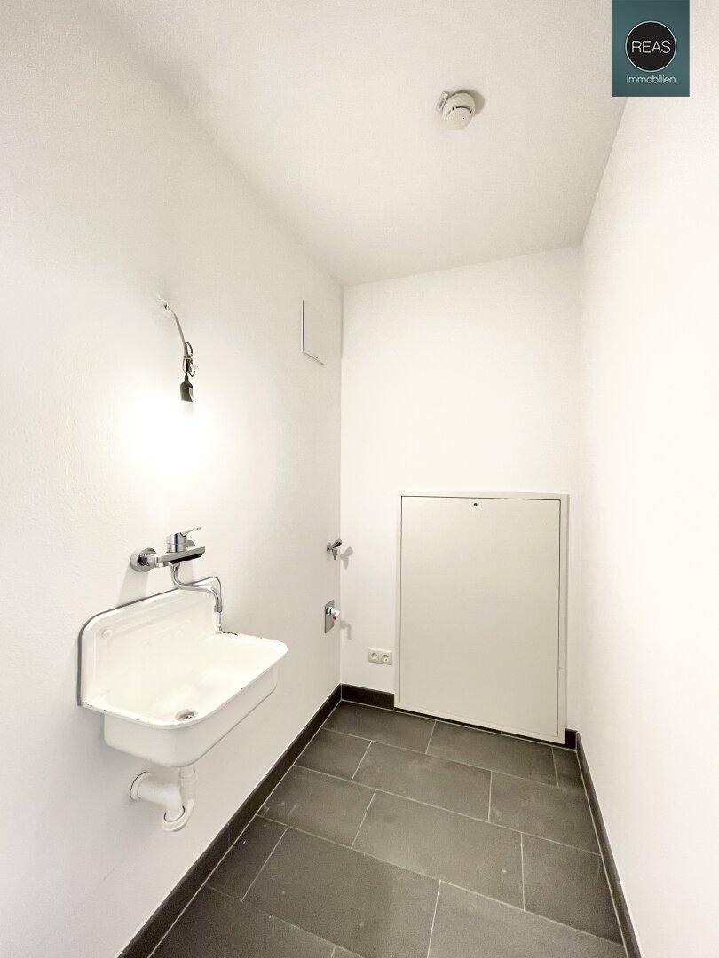 Kleiner Hauswirtschaftsraum mit Waschbecken und dunklen Fliesen, ideal für praktische Zwecke.