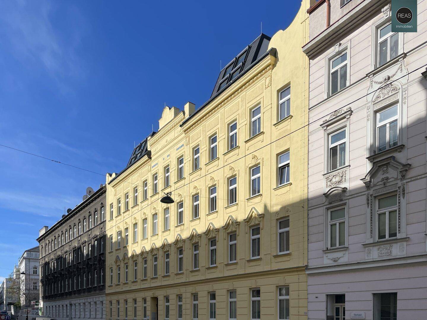 Historische gelbe Fassade eines Wohngebäudes an einer Straße unter blauem Himmel.