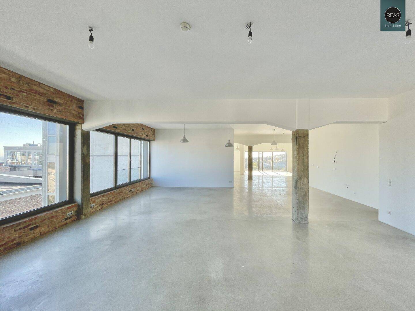 Heller, leerer Büroraum mit Betonboden und großen Fenstern, die viel Tageslicht hereinlassen und einen weiten Blick bieten.