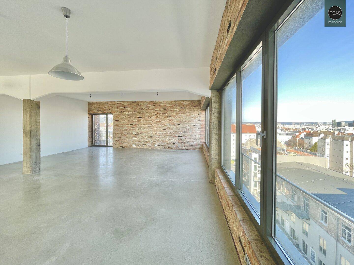 Langer, leerer Büroraum mit Betonboden und einer Reihe großer Fenster, die einen Panoramablick auf die Stadt bieten.