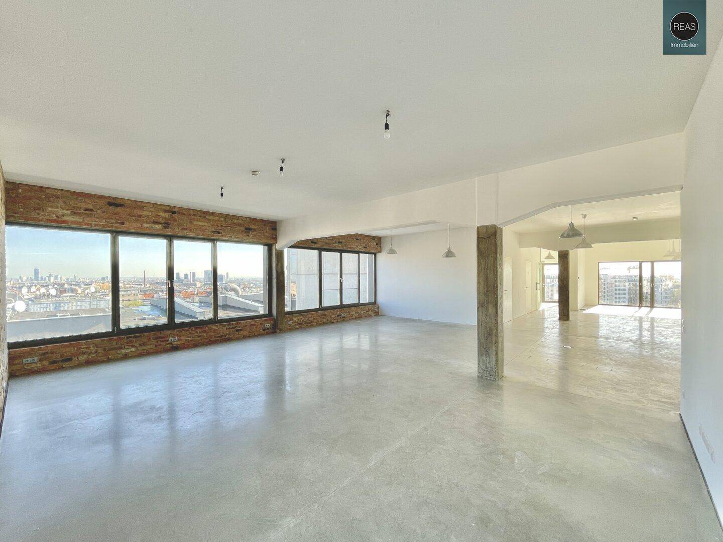 Weitläufiger, leerer Büroraum mit Betonboden und großen Fenstern, die einen Panoramablick auf die Stadt bieten.