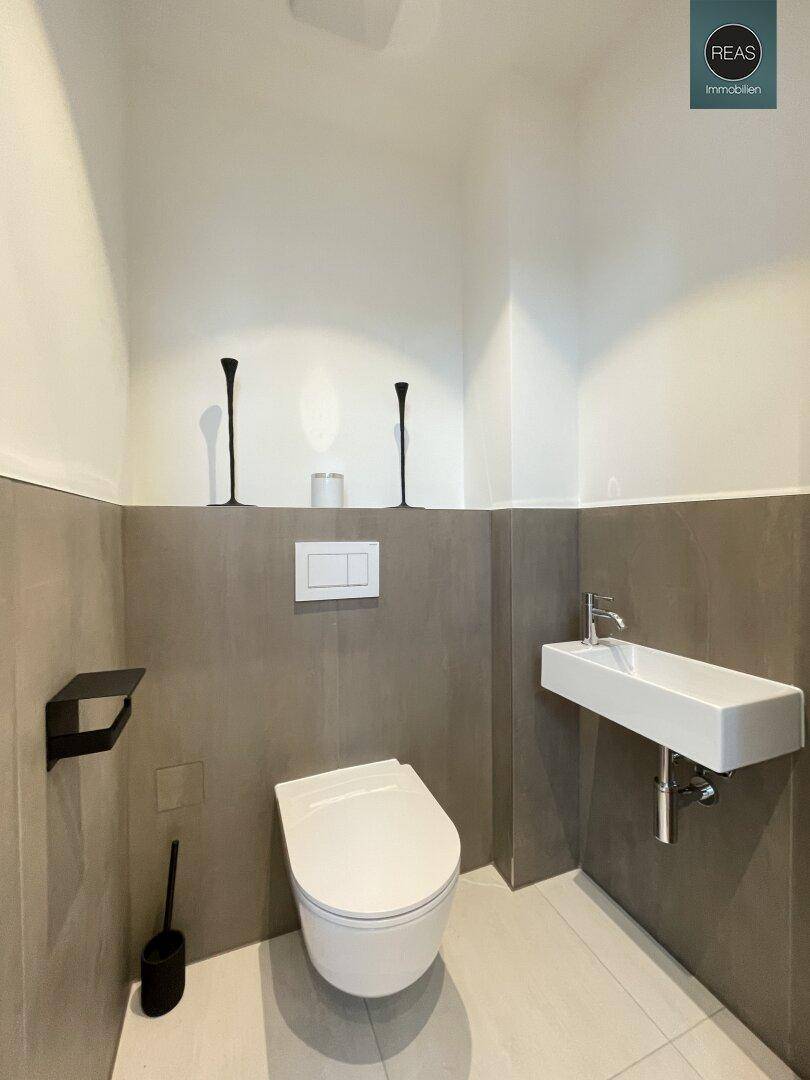 Modernes Gäste-WC mit Wand-WC, kleinem Waschbecken und grauen Wandfliesen.