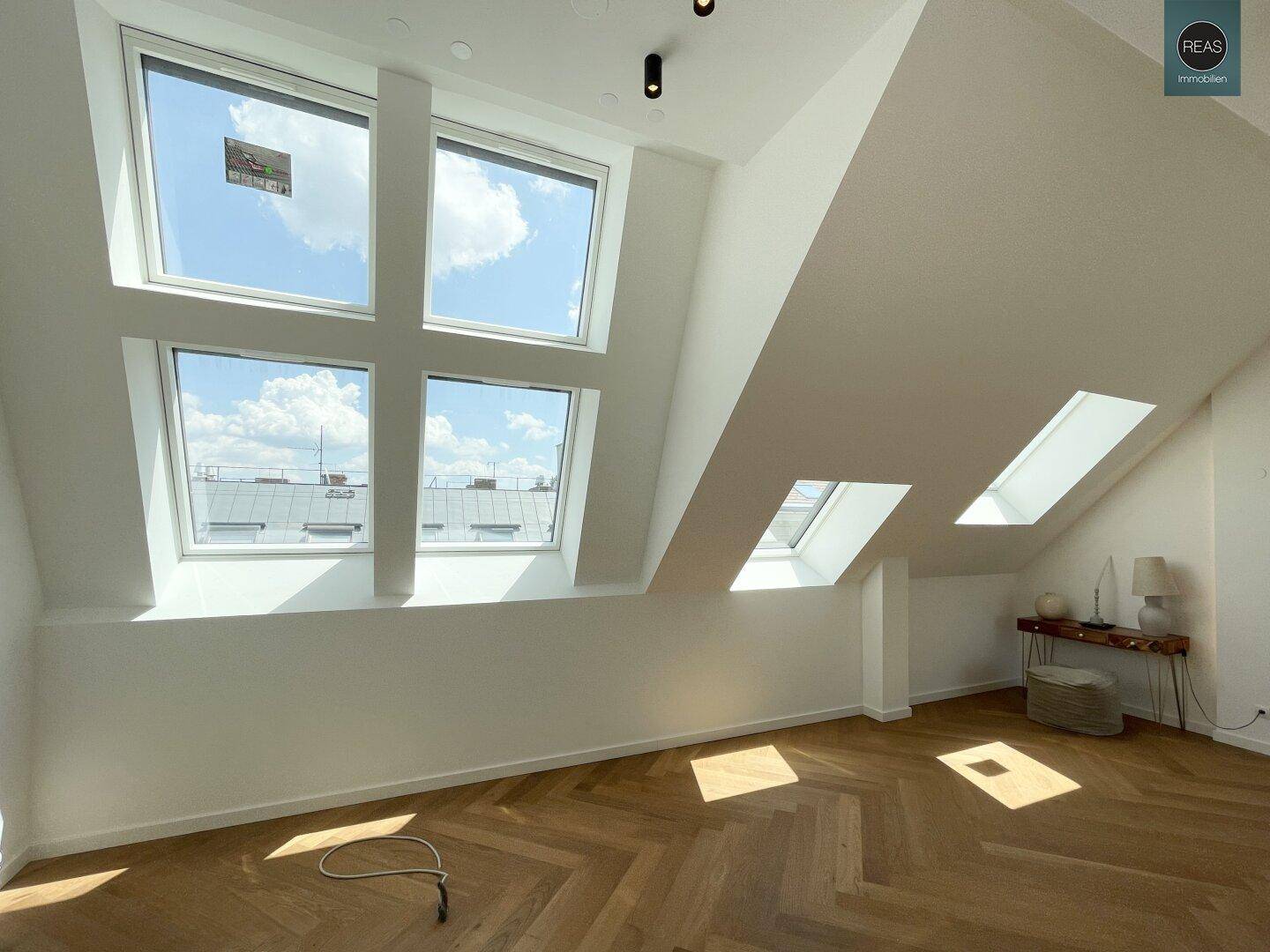 Heller Wohnraum im Dachgeschoss mit großen Fenstern und Blick auf den Himmel.