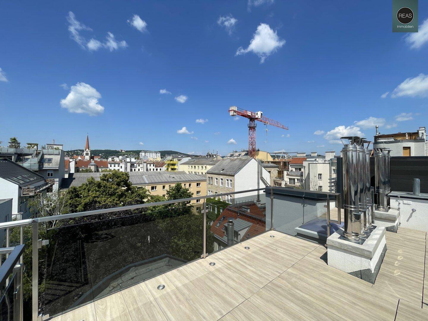 Dachterrasse mit Stadtblick und moderner Glasbrüstung unter blauem Himmel.