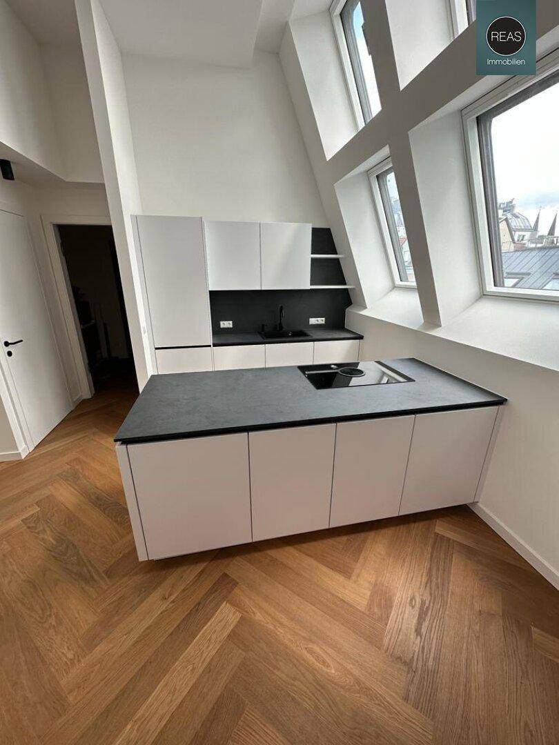 Moderne Einbauküche mit Kochinsel, dunkler Arbeitsplatte und großen Dachfenstern.