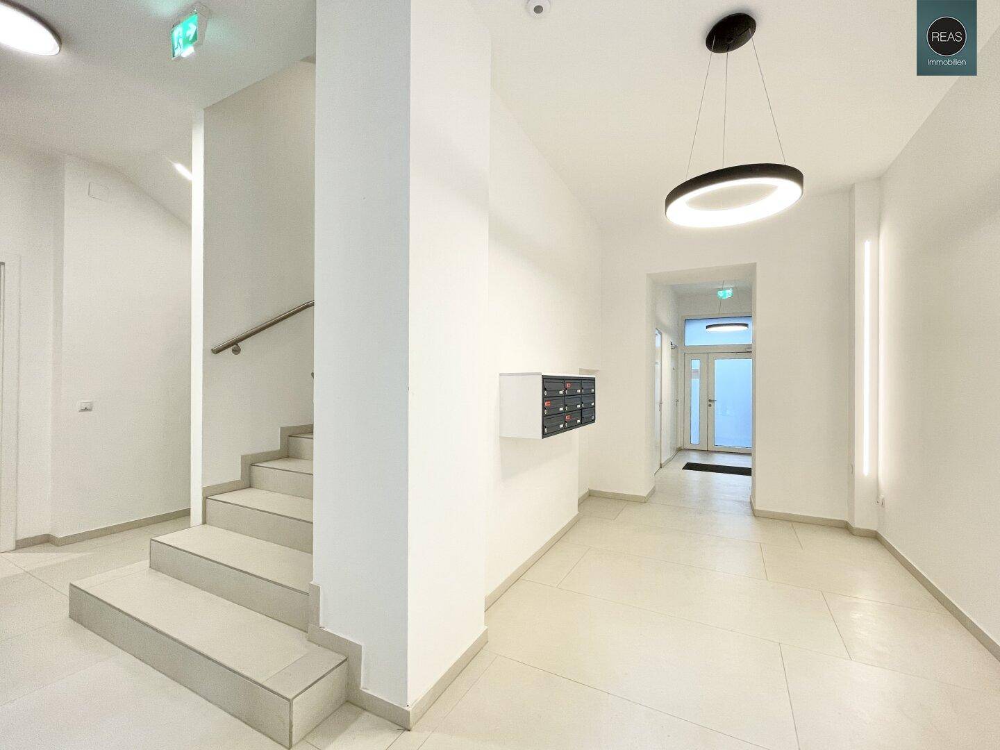Heller Eingangsbereich des Gebäudes mit Treppe und Briefkästen in modernem Design.