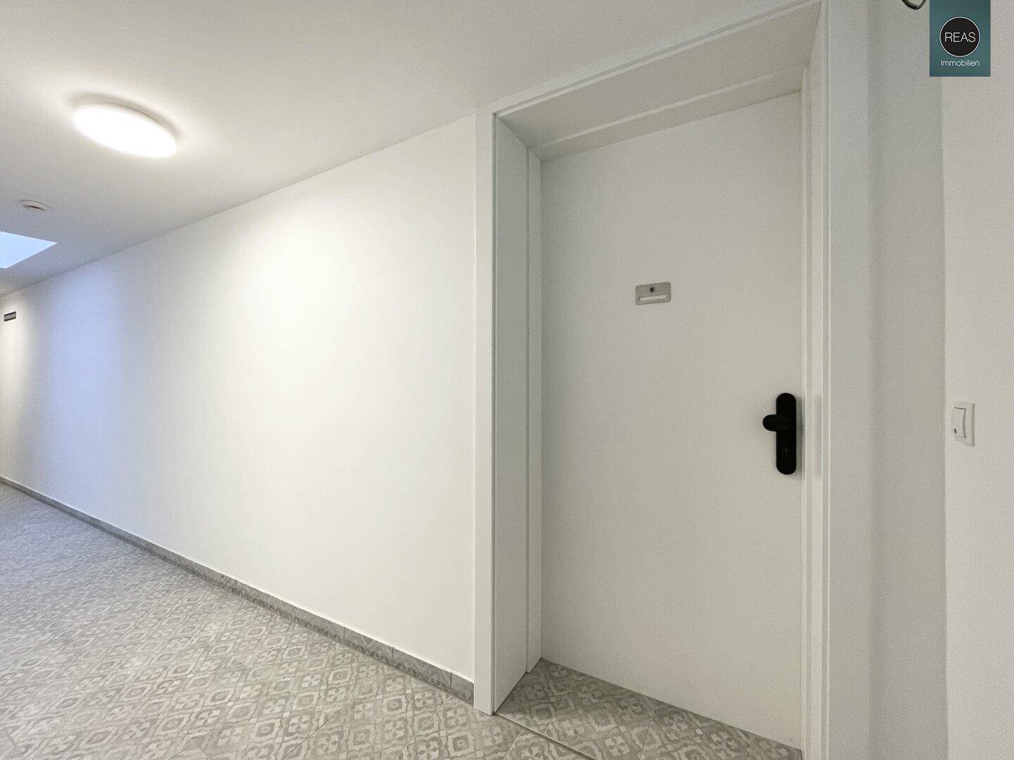 Heller Flur mit weißer Tür und gemustertem Fliesenboden in einem Mehrfamilienhaus.