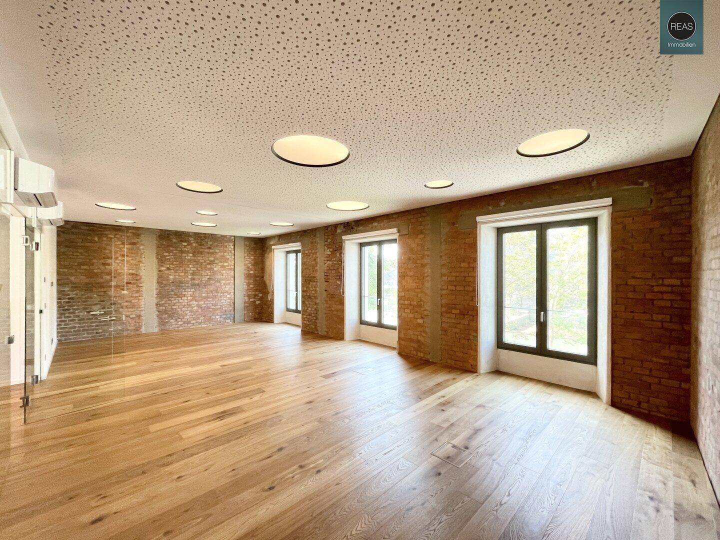 Heller Büroraum mit freigelegten Ziegelwänden, Holzboden und moderner Deckenbeleuchtung.