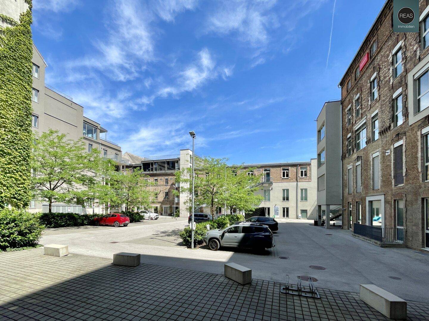 Heller Innenhof mit gepflasterten Wegen, parkenden Fahrzeugen und der Architektur des Gebäudekomplexes.