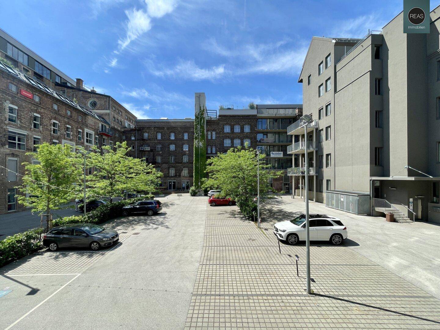 Weitläufiger Innenhof mit gepflasterten Flächen, parkenden Autos und modernen sowie historischen Gebäuden.
