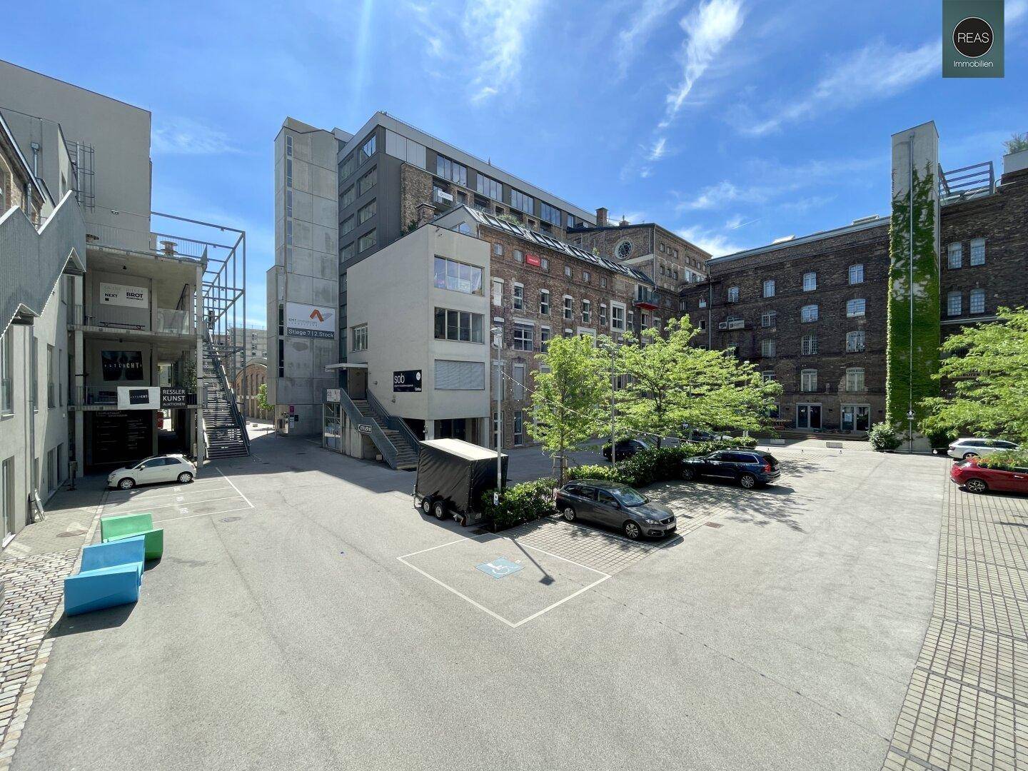 Innenhofansicht mit verschiedenen Gebäudestilen, Parkplätzen und einem modernen Treppenaufgang.