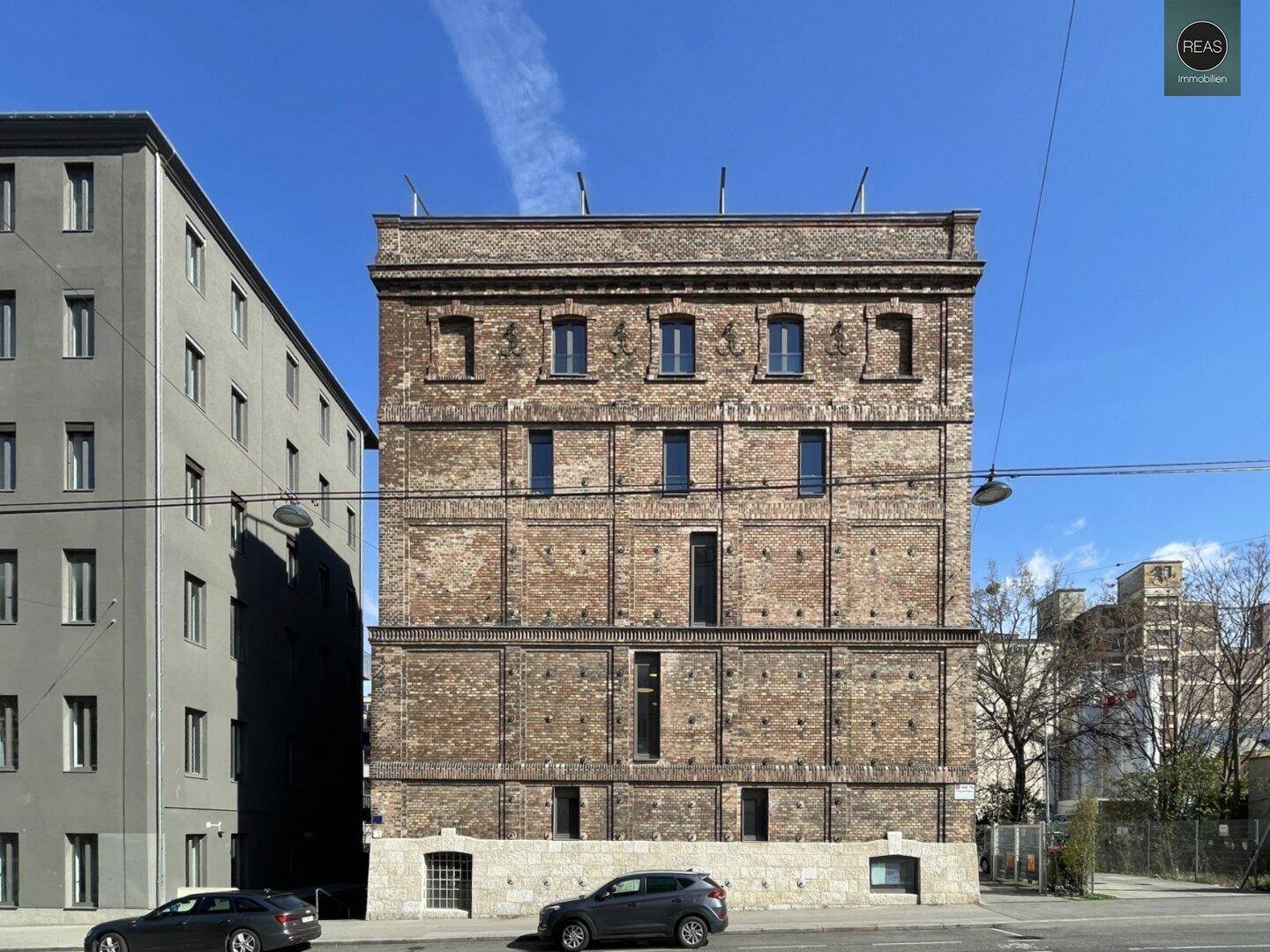 Frontale Ansicht des historischen Backsteingebäudes mit schmalen Fenstern und geparkten Autos davor.