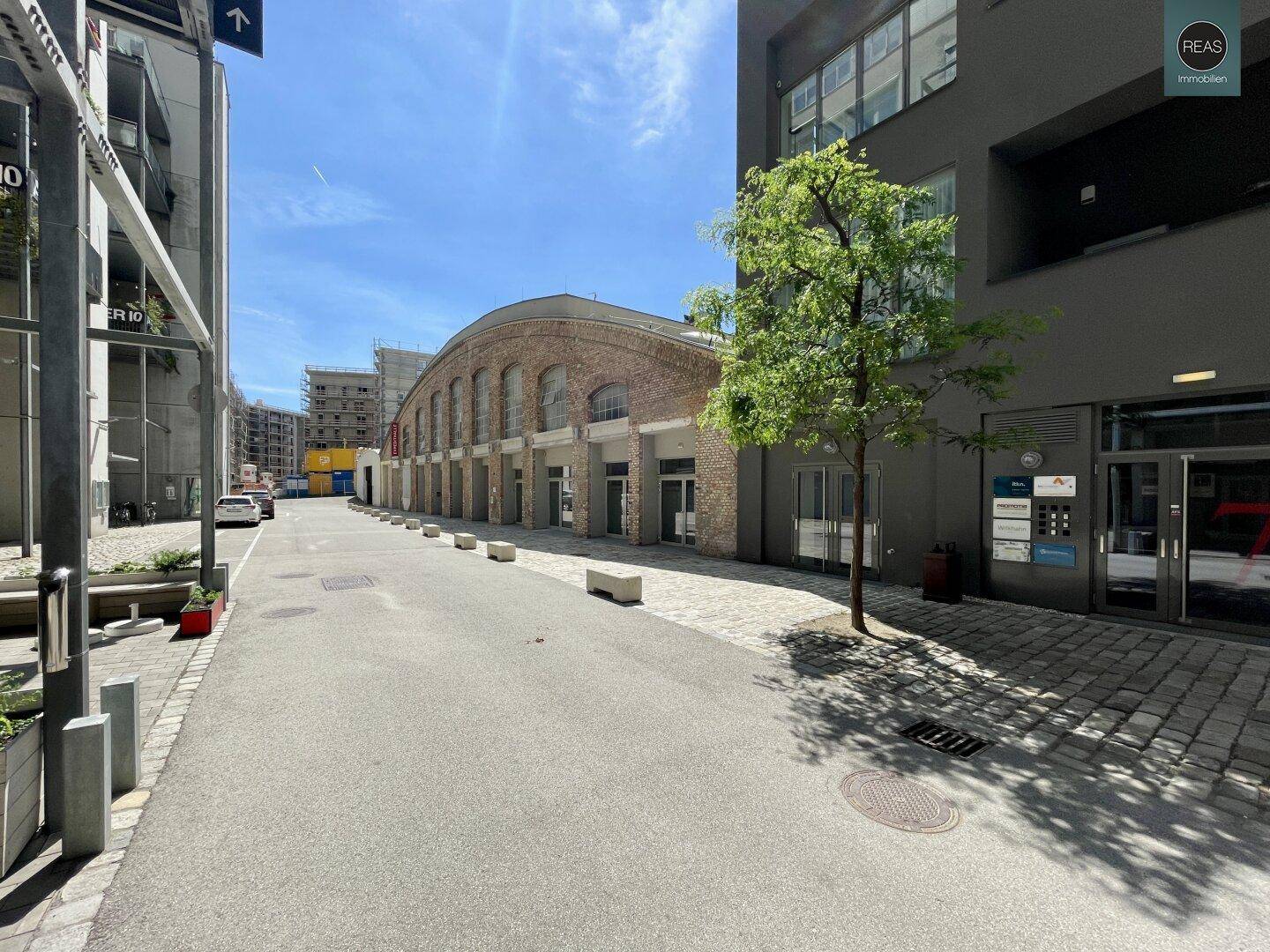Straßenansicht mit einem geschwungenen Backsteingebäude im Hintergrund und modernen Gebäuden an den Seiten.