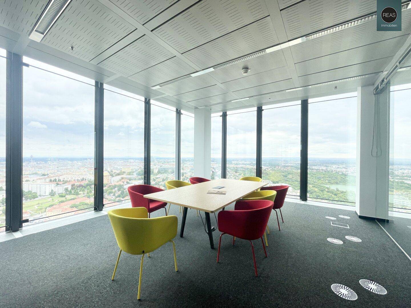 Moderner Konferenzraum mit farbigen Stühlen und einem Holztisch, bietet einen beeindruckenden Stadtblick.